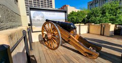 Replica of 18 pounder cannon on a carriage in front of a Defender of the Alamo panel