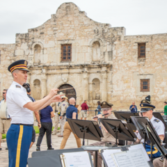Army conductor leading a group of army musicians seated to the side of Alamo Church