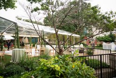 Round tables and rustic wood chairs set out in Alamo Gardens for an event by a large tent