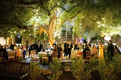Guests seated at round tables at an event in the gardens with string lights in the trees