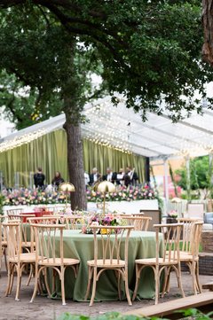 Round table with sage linens and floral centerpiece in front of an outdoor event tent