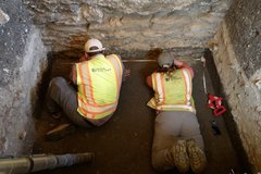 Two archaeologists cleaning the wall inside an excavation unit