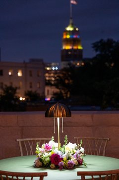 Spring florals with a small lamp on a green linen on a cocktail table outside on the terrace with a city view