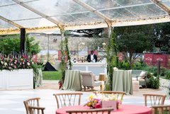 Dance floor of an outdoor tent with florals by the stage and a bar