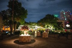 Cocktail tables set out at outdoor event in Alamo Gardens with a large tent and string lighting