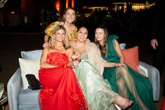 Four ladies in gowns seated on a blue couch at an outdoor garden event at night