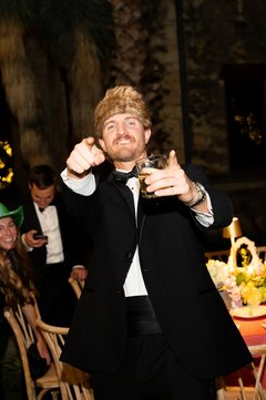 Man in a tuxedo wearing a coonskin cap pointing with both hands