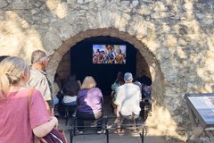 Guests seated on benches watching a film in the Alamo Long Barrack